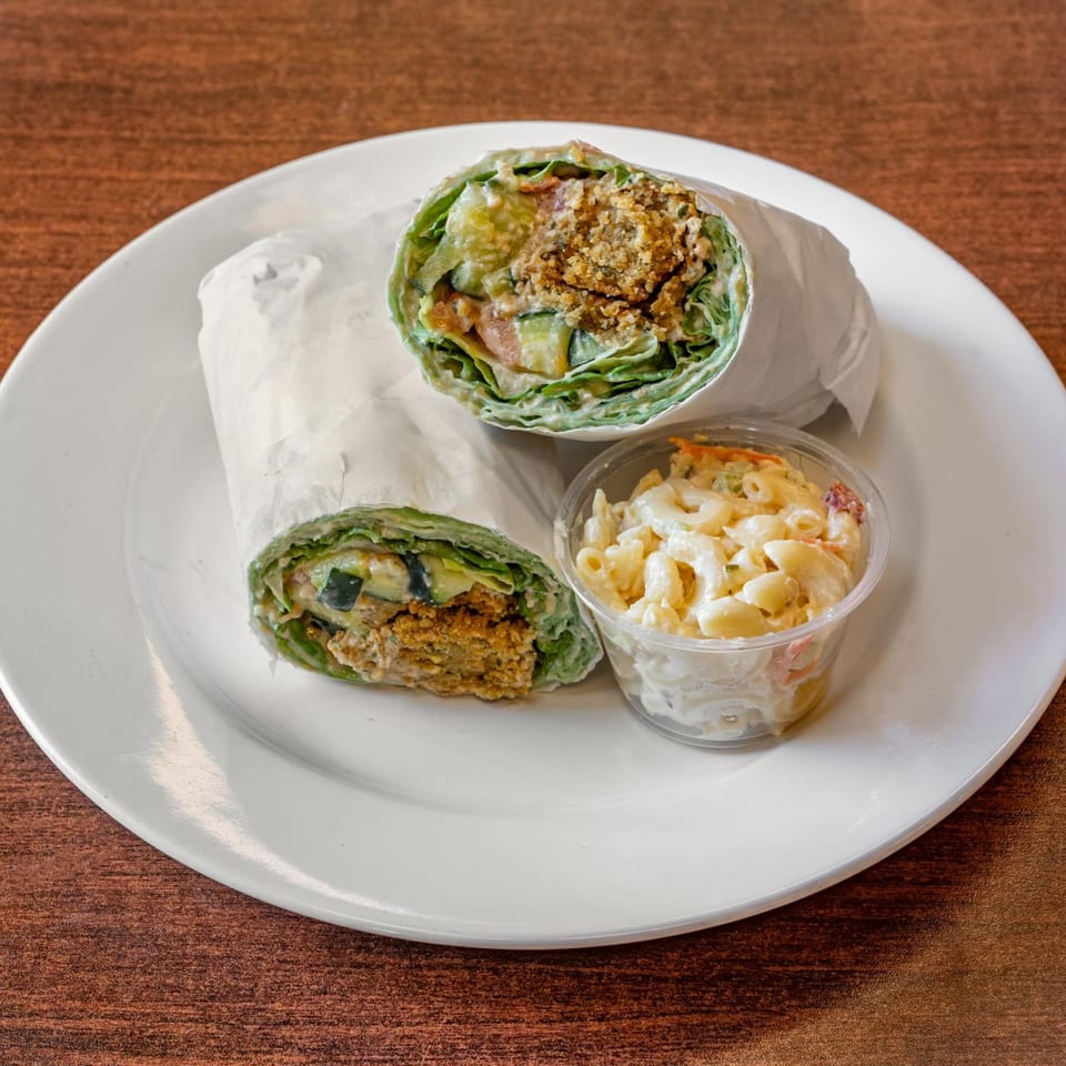 Two halves of a falafel wrap with lettuce, cucumber, and sauce, served with macaroni salad.