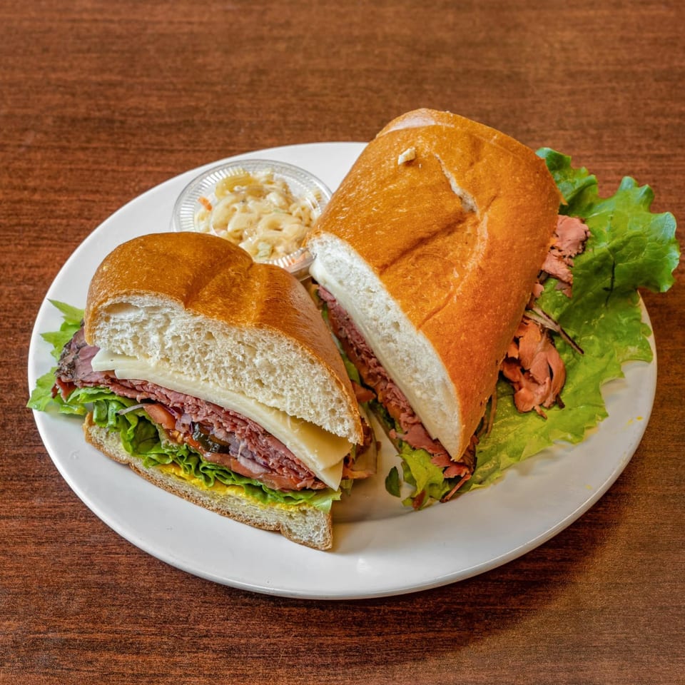 A roast beef sandwich on a baguette, cut in half, served with macaroni salad.
