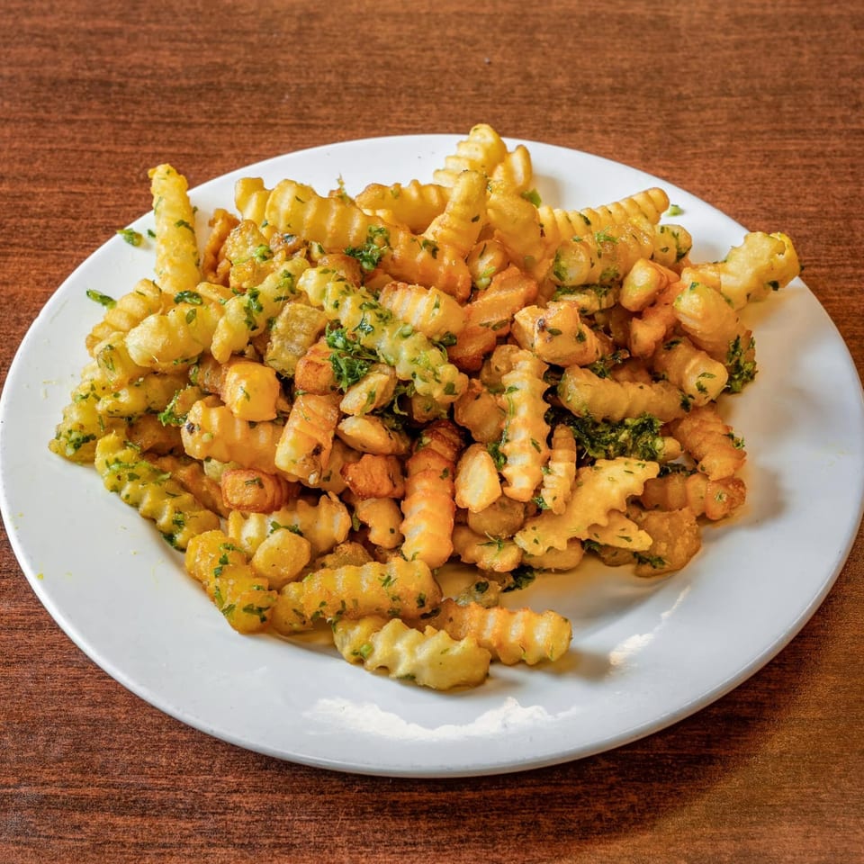A white plate filled with golden crinkle-cut fries, generously seasoned with green herbs.