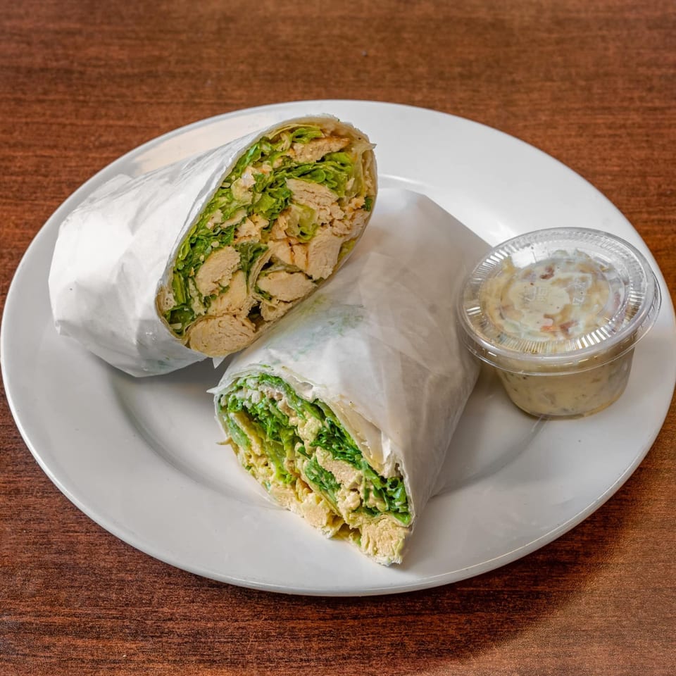 Two chicken Caesar wraps, cut in half, with a side of potato salad on a white plate.