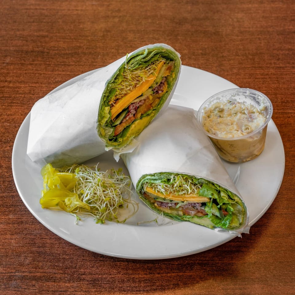 Two green wraps, cut in half, with sprouts, cheese, and vegetables, served with a side of dip.